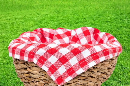 Empty picnic basket. Close-up of a empty straw basket therein a red checkered napkin isolated on a green grass background. For your food and product display montage. Macro.