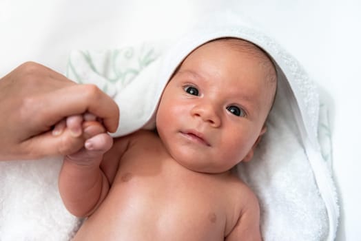 Adorable 2 months old little baby boy on towel after bath holding his mother's hand