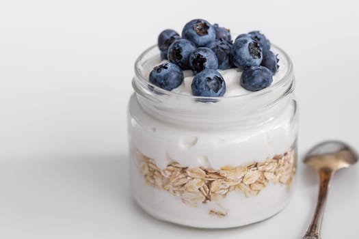 Thick yogurt with oatmeal in a glass jar decorated with fresh blueberries, light breakfast
