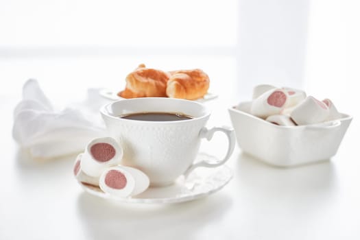 Sweet meal. Dessert. Still life with cup of coffee and bowls with marshmallows and croissants on light background.