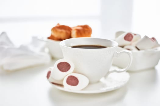 Sweet meal. Dessert. Still life with cup of coffee and bowls with marshmallows and croissants on light background.