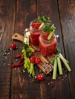 Two glasses with fresh tomato juice, celery, parsley, spices and ripe tomatoes on dark brown wooden background. Top view. Healthy beverage, vegetable juice