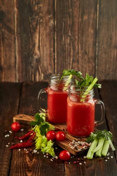Two glasses with fresh tomato juice, celery, parsley, spices and ripe tomatoes on dark brown wooden background with copy space. Healthy beverage, vegetable juice