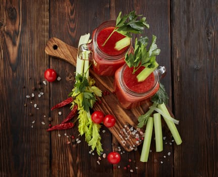 Two glasses with fresh tomato juice, celery, parsley, spices and ripe tomatoes on dark brown wooden background. Top view. Healthy beverage, vegetable juice