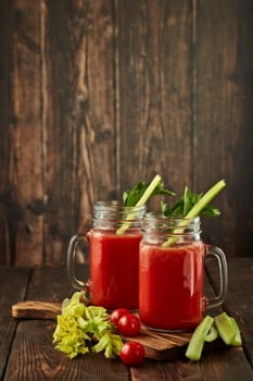 Two glasses with fresh tomato juice, celery, parsley and ripe tomatoes on dark brown wooden background. Healthy beverage, vegetable juice