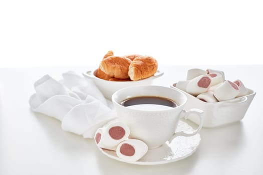 Sweet meal. Dessert. Still life with cup of coffee and bowls with marshmallows and croissants on white background.