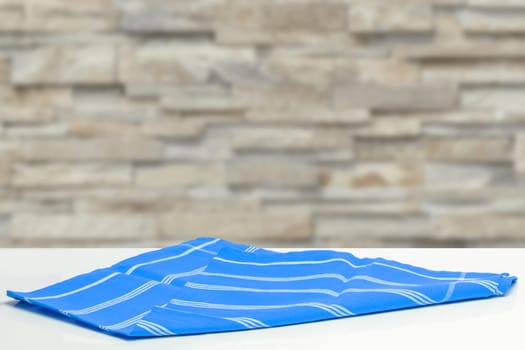 Closeup of a empty blue striped tablecloth or napkin on a bright table against abstract blurred wall background. Template for food and product display montage.