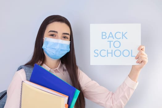 High school girl with mask on her showing back to school message. Student girl ready for school during the coronavirus pandemic. Focus on her face.