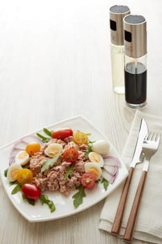 Tuna salad with arugula and tomatoes on white plate on light wooden background. Healthy food, seafood menu, Setting table