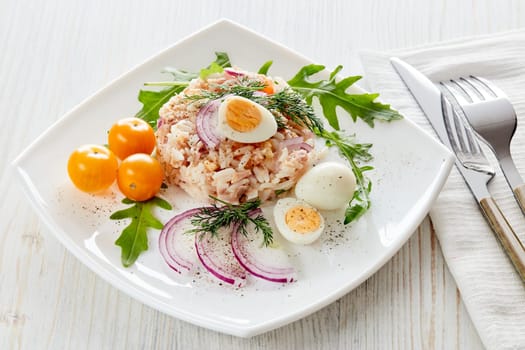 Tuna salad with  rice, arugula and tomatoes on white plate on light wooden background. Top view. Healthy food, seafood menu, Setting table