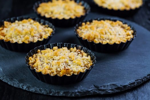 Small and delicious apple pies or apple crumble on black background. Apple tart.