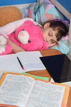 Girl fell asleep in a hug with a teddy bear doing lessons at home
