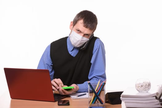 An office worker in a protective medical mask is talking on the phone, counting on a calculator and looking at the frame