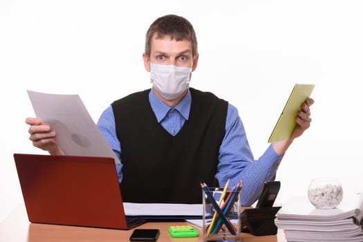 A man in a medical mask holds a paper document in one hand, and a tablet computer in the other