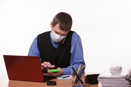 An office employee in a protective medical mask is talking on the phone, counting on a calculator