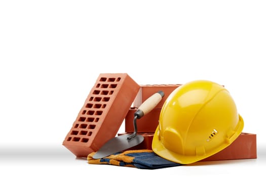 Construction concept. Stack of new bricks with masonry trowel, construction yellow hard hat and protective  gloves on white background with copy space.