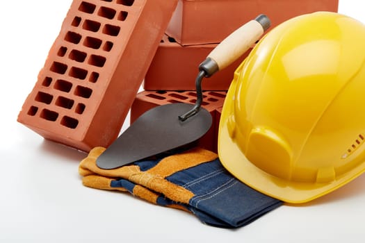 Construction concept. Stack of new bricks with masonry trowel, construction yellow hard hat and protective  gloves on white background.