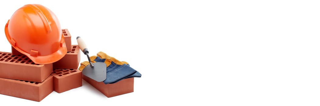 Construction concept. Stack of new bricks with masonry trowel, construction orange hard hat and protective  gloves on white background. Extra wide panorama banner.