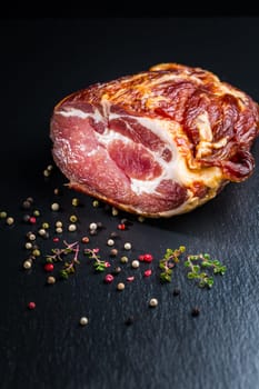 Piece of smoked ham with pepper and herbs on black background. Traditional smoked pork meat.
