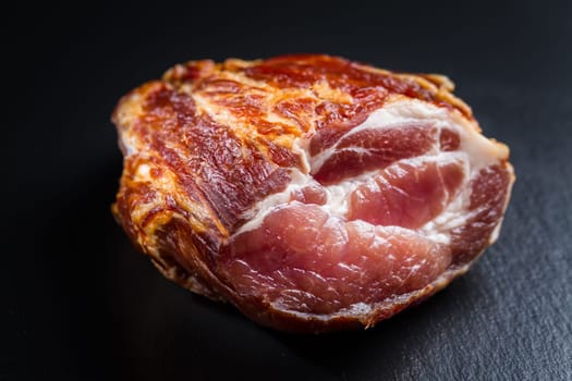 Piece of smoked ham with pepper and herbs on black background. Traditional smoked pork meat.