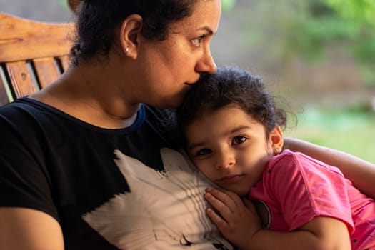 Mother and young child sit on rock chair and enjoying together at outdoor balcony, togetherness concept in golden light