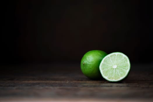 Whole and half lime on wooden surface with copy space.