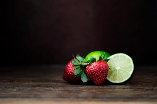 Strawberries and lime on dark wooden surface with dark background. Space for copy and/or compositing product
