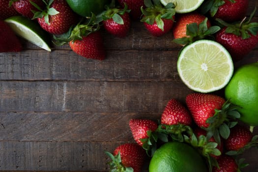 Flat lay of fresh lime and strawberries on dark wooden sufrace with copy space
