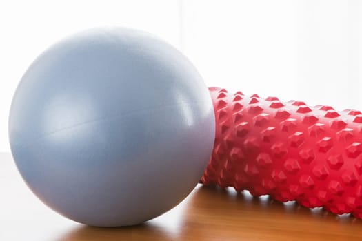 A blue pilates ball and a red fascial massage roller with backlight and wooden floor