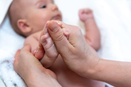 Adorable 2 months old little baby boy on towel after bath holding his mother's hands