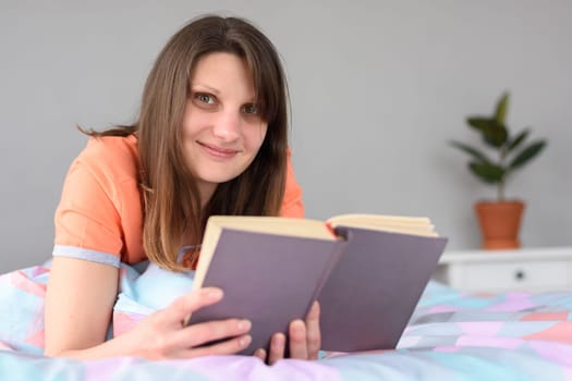 The girl reads a book and looked into the frame with a smile
