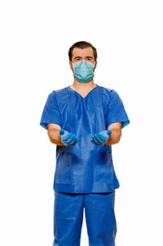 Male doctor in scrubs with protective face mask and gloves, reaching out with open hands on plain white background. Coronavirus or covid 19 concept