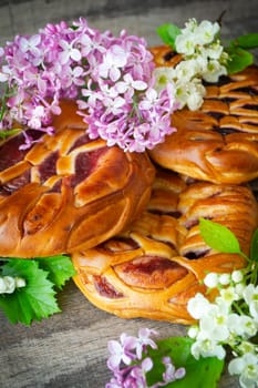 Homemade yeast pie with jam on a wooden table with spring lilac and white flowers. Vertical image