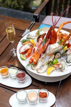 Bowl of gourmet fresh seafood on ice with savory sauce serve with white wine glass on vintage wooden table. Restaurant gastronomy food and drink consumerism concept.