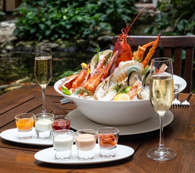 Bowl of gourmet fresh seafood on ice with savory sauce serve with white wine glass on vintage wooden table. Restaurant gastronomy food and drink consumerism concept.