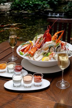 Bowl of gourmet fresh seafood on ice with savory sauce serve with white wine glass on vintage wooden table. Restaurant gastronomy food and drink consumerism concept.