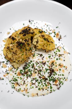 Roasted Cauliflower with Parmesan and Hazelnut topping with spring onion and cauliflower soup, gourmet international cuisine recipe. Restaurant gastronomy food and drink consumerism concept.