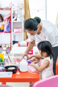 Asian girl kid playing toy and colorful paper for art lesson at living room in home as home schooling while city lockdown because of covid-19 pandemic across the world with quaratine mom as teacher.