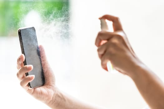 close-up cleaning mobile phone using alocohol spray from bottle spraying, disinfection for safety prevent and protect from infection of virus and germ Covid-19 coronavirus world pandemic.