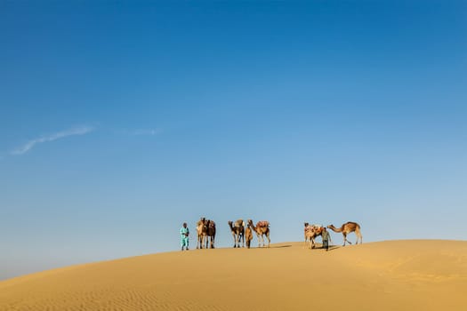 Rajasthan travel background - Three cameleers (camel drivers) with camels in dunes of Thar desert. Jaisalmer, Rajasthan, India