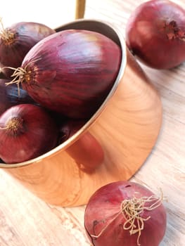 Red onions in a copper pan on a rustic wooden background
