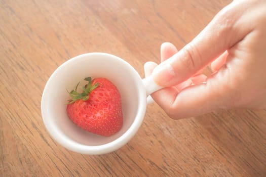 Single fresh ripe strawberry in white mug, stock photo