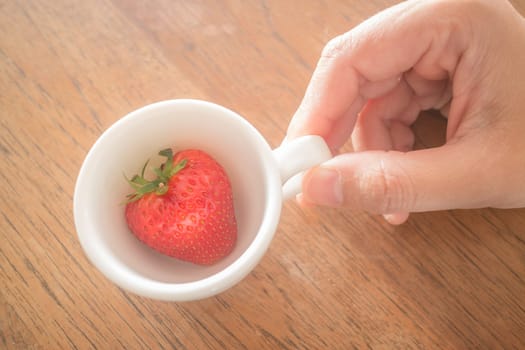 Single fresh ripe strawberry in white mug, stock photo