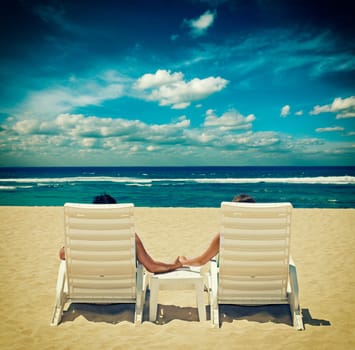 Couple in beach chairs holding hands near ocean