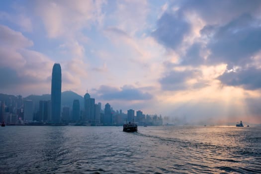 Hong Kong skyline cityscape downtown skyscrapers over Victoria Harbour on sunset with tourist ferry boat silhouette. Hong Kong, China