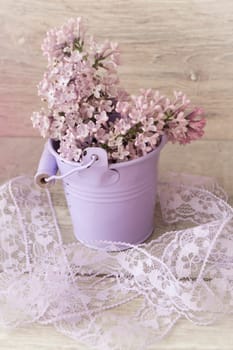 Blooming lilac bouquet in violet bucket on light wooden background. Vintage