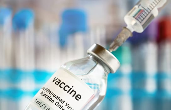 Vaccine glass bottle with syringe injected, blurred vials background.