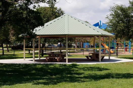 Pompano Beach, FL, USA - April 7, 2020: Pompano Beach Park showing caution sign tape around a pavilion with picnic tables. Cordoned off seating area due to Covid-19 pandemic government restrictions.