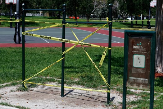Pompano Beach, FL, USA - April 7, 2020: Yellow and black caution tape blocking access to chin-up bars during the Covid-19 pandemic. Caution sign tape on exercise equipment during corona virus alert.
