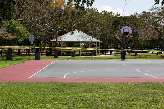 Pompano Beach, FL, USA - April 7, 2020: During the Covid-19 pandemic active sports including this basketball court were cordoned off with caution tape. Basketball court closed with caution barrier.